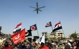 Des Syriens brandissent le drapeau national et celui du parti social nationaliste dans un stade au passage d'un hélicoptère russe Mil Mi-24 durant les funérailles du général de division Issam Zahreddine, dans la ville du sud de  Suwaida, le 20 octobre 2017 (Crédit :AFP /STRINGER)