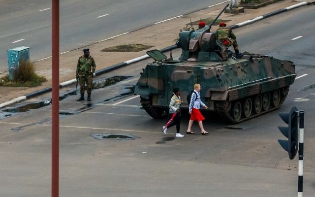 Des jeunes femmes devant un camion blindé à un carrefour, la circulation est gérée par des soldats zimbabwéens, à Harare, le 15 novembre 2017. (Crédit : AFP)