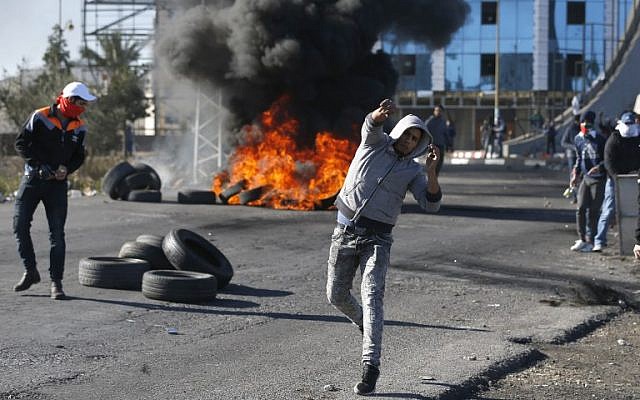 Des émeutiers palestiniens jettent des pierres sur les troupes israéliennes à un point de contrôle israélien près de la ville de Ramallah en Cisjordanie, le 8 décembre 2017 (Crédit : AFP / ABBAS MOMANI)