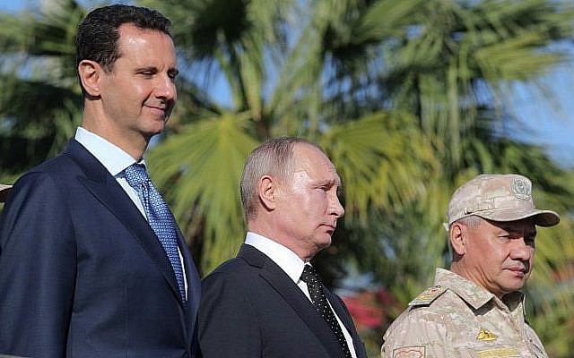 Le président syrien Bashar el-Assad, (à gauche), le président russe Vladimir Poutine et le ministre russe de la Défense Sergei Choigou inspectent un défilé militaire lors de leur visite à la base aérienne russe de Hmeimim, dans la province de Lattaquié, le 11 décembre 2017. (Crédit : Mikhail Klimentyev / AFP)