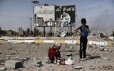 Cette photo prise le 12 mars 2017 montre des enfants irakiens assis dans les décombres d'une rue du quartier de Naplouse à Mossoul devant un tableau portant le logo de l'Etat islamique durant une offensive des forces de sécurité pour la reprise des quartiers ouest de la ville, aux mains de l'EI (Crédit : AFP PHOTO / ARIS MESSINIS)