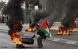 Un manifestant palestinien fait brûler un pneu durant des émeutes contre les forces de sécurité israélienne à Bethléem, en Cisjordanie, le 29 décembre 2017, après les prières du vendredi musulmanes (Crédit : AFP / Musa al Shaer)