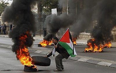 Un manifestant palestinien fait brûler un pneu durant des émeutes contre les forces de sécurité israélienne à Bethléem, en Cisjordanie, le 29 décembre 2017, après les prières du vendredi musulmanes (Crédit : AFP / Musa al Shaer)
