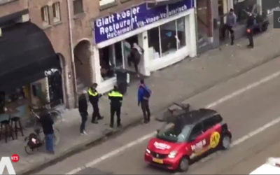Un homme portant keffieh et drapeau palestiniens brise la vitrine d'un restaurant casher à Amsterdam, le 7 décembre 2017 (Crédit : capture d'écran Télévision néerlandaise AT5)