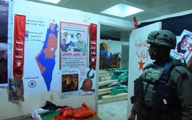 Un soldat israélien se tenant à côté de ce que l'armée a qualifié de "matériel d'incitation [au terrorisme]", saisi lors de raids nocturnes le 14 décembre 2017. (Crédit : Armée israélienne)
