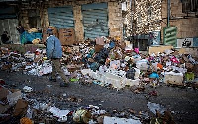 Les clients passent devant des piles d'ordures laissées par des ouvriers de la ville en grève, au Marché Mahane Yehuda de Jérusalem, le 7 janvier 2018. (Yonatan Sindel / Flash90)
