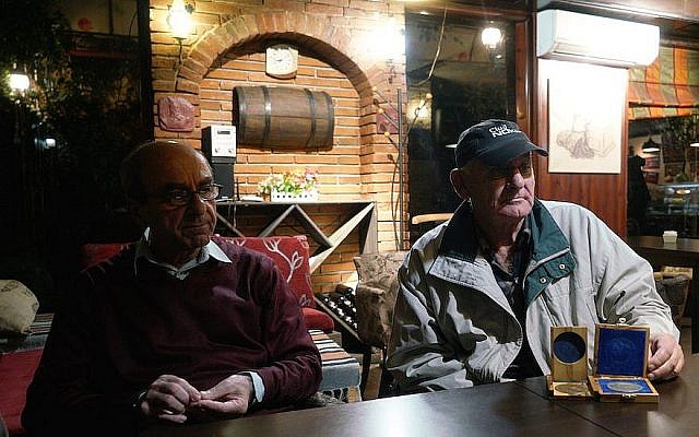 Rexhep Hoxha, à gauche, et Fatos Qoqja dans un bar à Tirania, en Albanie, le 8 novembre 2017. Qoqja est photographiée avec la médaille que son père a reçue pour avoir sauvé des Juifs pendant l'Holocauste. (Crédit : Cnaan Liphshiz / via JTA)
