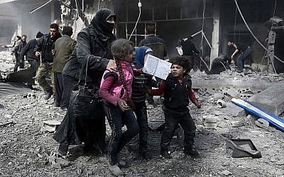 Une femme syrienne et des enfants courent pour trouver un abri   après un bombardement gouvernemental dans la ville d' Hammuriyeh, détenue par les rebelles,  à la Ghouta orientale, détenue par les rebelles, aux abords de Damas, le 19 février 2018 (Crédit :  AFP PHOTO /Abdulmonan Eassa)