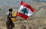 Un membre du groupe terroriste du Hezbollah tient des drapeaux libanais et du Hezbollah lors d'un voyage de presse près de la ville frontalière d'Arsal, le 25 juillet 2017. (Photo AFP / Stringer)