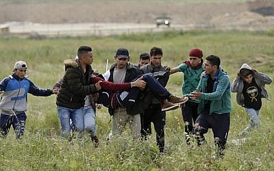 Un jeune Palestinien blessé est porté par d'autres manifestants alors qu'ils fuient lors d'affrontements à la frontière avec Israël à l'est de la ville de Gaza commémorant la Journée de la Terre, le 30 mars 2018 (Crédit : AFP PHOTO / MAHMUD HAMS)