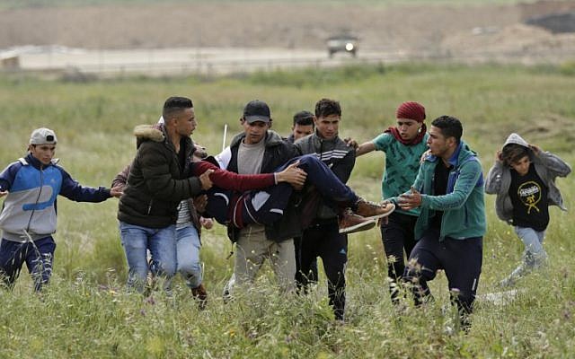 Un jeune Palestinien blessé est porté par d'autres manifestants alors qu'ils fuient lors d'affrontements à la frontière avec Israël à l'est de la ville de Gaza commémorant la Journée de la Terre, le 30 mars 2018 (Crédit : AFP PHOTO / MAHMUD HAMS)