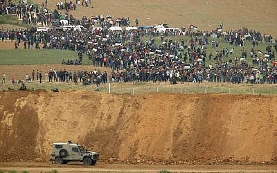 Une photo prise le 30 mars 2018 du kibboutz israélien sud de Nahal Oz de l'autre côté de la bande de Gaza montre des Palestiniens participant à une manifestation pour commémorer la Journée de la Terre, avec des véhicules militaires israéliens au premier plan (Crédit : AFP PHOTO / Jack GUEZ)