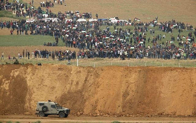Une photo prise le 30 mars 2018 du kibboutz israélien sud de Nahal Oz de l'autre côté de la bande de Gaza montre des Palestiniens participant à une manifestation pour commémorer la Journée de la Terre, avec des véhicules militaires israéliens au premier plan (Crédit : AFP PHOTO / Jack GUEZ)