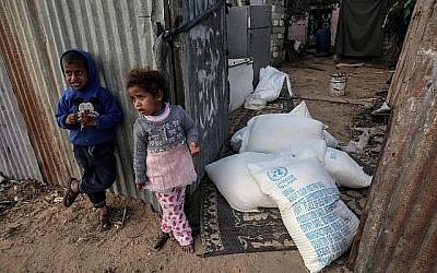 Des enfants palestiniens se tiennent à côté de sacs d'aide alimentaire fournis par l'agence des Nations Unies pour les réfugiés palestiniens dans le camp de réfugiés de Rafah, dans le sud de la bande de Gaza, le 24 janvier 2018. (Crédit : AFP/Said Khatib)