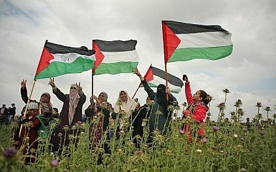 Des femmes palestiniennes brandissent des drapeaux et font le signe de la victoire durant une manifestation aux abords de la frontière avec Israël, à l'est de Jabalia, dans la bande de Gaza, le 30 mars 2018 (Crédit : AFP PHOTO / Mohammed ABED)