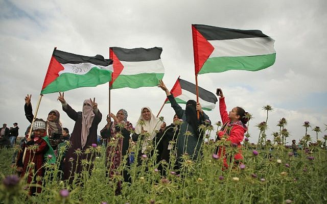 Des femmes palestiniennes brandissent des drapeaux et font le signe de la victoire durant une manifestation aux abords de la frontière avec Israël, à l'est de Jabalia, dans la bande de Gaza, le 30 mars 2018 (Crédit : AFP PHOTO / Mohammed ABED)