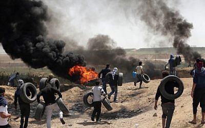 Des hommes palestiniens collectent des pneus et les brûlent pour se protéger des tirs de soldats israéliens à la frontière entre Israël et Gaza lors d'une manifestation à l'est de la ville de Gaza, le 6 avril 2018 (Crédit : AFP PHOTO / MAHMUD HAMS)