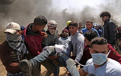 Des hommes palestiniens transportent un manifestant blessé après des affrontements avec les forces israéliennes à la frontière entre Israël et Gaza lors d'une manifestation, à l'est de la ville de Gaza, dans la bande de Gaza, le 6 avril 2018 (Crédit : PHOTO AFP / MAHMUD HAMS)