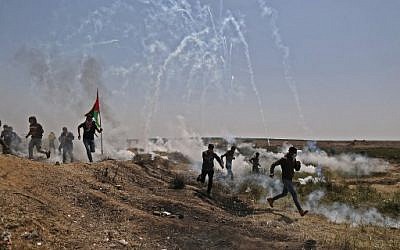 Des hommes palestiniens se cachent sous les bombes à gaz à la frontière entre Israël et Gaza lors d'une manifestation, à l'est de la ville de Gaza, dans la bande de Gaza, le 6 avril 2018 (Crédit : PHOTO AFP / MAHMUD HAMS)
