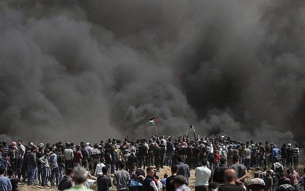 Des Palestiniens brandissent leurs drapeaux sous une forte fumée de pneus brûlés par les Gazaouis à la frontière entre Israël et Gaza lors d'une manifestation, à l'est de la ville de Gaza, le 6 avril 2018 (AFP PHOTO / MAHMUD HAMS) Des Palestiniens brandissent leurs drapeaux sous une forte fumée de pneus brûlés par les Gazaouis à la frontière entre Israël et Gaza lors d'une manifestation, à l'est de la ville de Gaza, le 6 avril 2018 (AFP PHOTO / MAHMUD HAMS)