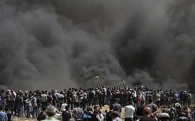 Des Palestiniens brandissent leurs drapeaux sous une forte fumée de pneus brûlés par les Gazaouis à la frontière entre Israël et Gaza lors d'une manifestation, à l'est de la ville de Gaza, le 6 avril 2018 (AFP PHOTO / MAHMUD HAMS)