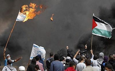 Des manifestants palestiniens brûlent des drapeaux israéliens près de la barrière frontalière avec Israël, à l'est de Khan Yunis dans le sud de la ville de Gaza, le 13 avril 2018 (Crédit : AFP / Thomas Coex)