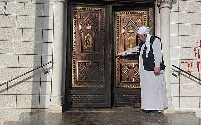 Un imam dans une mosquée du village palestinien d'Aqraba, dans le nord de la Cisjordanie, montre les dégâts causés par un incendie criminel survenu le 13 avril 2018. (Crédit : Zacharia Sadeh / Rabbis for Human Rights)