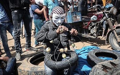 Un Palestinien portant un masque enfile des oignons sur un fil pour réduire les effets des gaz lacrymogènes lors des manifestations à la frontière entre Israël et Gaza près de Khan Yunis, à l'est de la ville de Gaza, le 6 avril 2018 (Crédit : AFP PHOTO / SAID KHATIB)