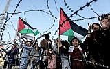 Une fille brandit un drapeau palestinien alors qu'un autre garçon palestinien tient une clé en bois symbolisant le retour, alors qu'ils se tiennent aux côtés d'autres personnes devant le fil barbelé marquant la frontière entre la bande de Gaza et Israël à l'est de la ville de Gaza le 13 mai 2018. (AFP/Mahmud Hams)