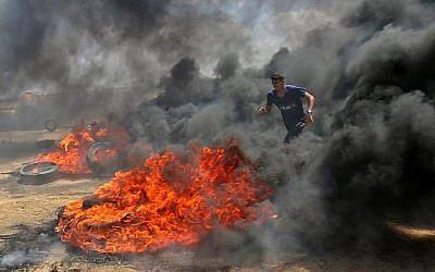 Un Palestinien marche dans la fumée dégagée par des pneus en feu durant des affrontements avec les forces israéliennes le long de la frontière avec la bande de Gaza, à l'est de  Khan Younis, le 14 mai 2018 (Crédit :  AFP PHOTO / SAID KHATIB)