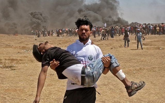 Un Palestinien transporte un blessé durant des affrontements avec l'armée israélienne entre la bande de Gaza et Israël, à l'est de Gaza City, le 14 mai 2018 (Crédit :  AFP / MAHMUD HAMS)