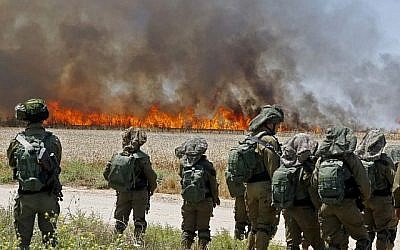 Des soldats israéliens face à un champ de blé en feu près du kibboutz Nahal Oz, incendié  par des cerfs-volants lancés par des émeutiers palestiniens depuis Gaza, le 14 mai 2018. (Crédit : JACK GUEZ/AFP)