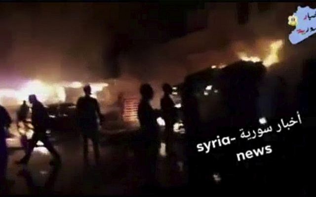 Cette capture d’écran tirée d’une vidéo fournie le 9 mai 2018 par l’agence Syria News montre des personnes debout devant les flammes réveillées après une attaque contre une zone connue pour héberger de nombreuses bases militaires de l'armée syrienne, à Kisweh, au sud de Damas, en Syrie. Mardi. l’Observatoire syrien des droits de l'homme basé en Grande-Bretagne a déclaré que les tirs ciblaient les dépôts et les armes qui appartenaient probablement aux forces iraniennes à Kisweh (Syria News)