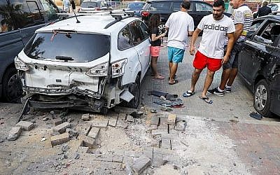 Des hommes israéliens se tiennent à côté d'une voiture qui a été endommagée après qu'une roquette tirée par des terroristes de la bande de Gaza soit tombée dans la ville de Sderot, dans le sud d'Israël, le 9 août 2018. (AFP PHOTO / JACK GUEZ)