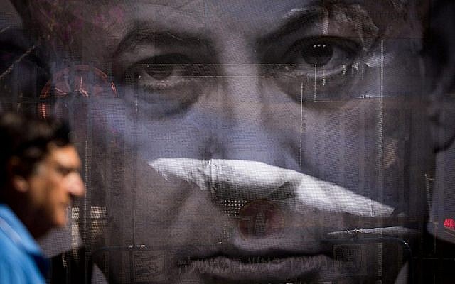 Un homme passe devant une affiche critiquant le Premier ministre Benjamin Netanyahu près de sa résidence à Jérusalem, alors que les enquêteurs de la police arrivent pour l'interroger sur des allégations de corruption, le 10 juillet 2018. (Yonatan Sindel/Flash90)