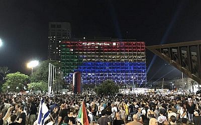Le drapeau druze illuminé dans la municipalité de Tel Aviv alors que les manifestants brandissent les drapeaux israéliens et druzes sur la place Rabin lors d'un rassemblement contre la loi sur l'Etat-nation, le 4 août 2018 (Crédit : Luke Tress / Times of Israel staff)