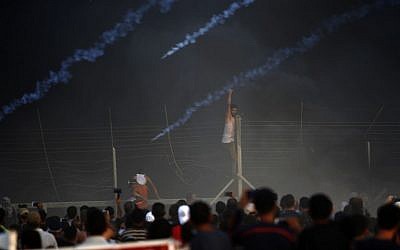 Un manifestant palestinien grimpe sur une clôture au cours d'une manifestation nocturne le long de la frontière entre Israël et Gaza parmi les fumées des pneus brûlés et les gaz lacrymogènes, le 14 septembre 2018 (Crédit :  / AFP PHOTO / Said KHATIB)