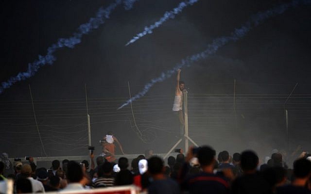 Un manifestant palestinien grimpe sur une clôture au cours d'une manifestation nocturne le long de la frontière entre Israël et Gaza parmi les fumées des pneus brûlés et les gaz lacrymogènes, le 14 septembre 2018 (Crédit : / AFP PHOTO / Said KHATIB) Un manifestant palestinien grimpe sur une clôture au cours d'une manifestation nocturne le long de la frontière entre Israël et Gaza parmi les fumées des pneus brûlés et les gaz lacrymogènes, le 14 septembre 2018 (Crédit : / AFP PHOTO / Said KHATIB)
