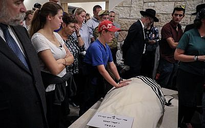 Le fils d'Ari Fuld place ses mains sur le corps de son père pendant ses funérailles à Kfar Etzion, le 17 septembre 2018 (Crédit : Gershon Elinson/FLASH90)