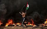 Un Palestinien tient un drapeau palestinien alors qu'il utilise une fronde pour lancer des pierres sur les troupes israéliennes lors d'affrontements près de la frontière avec Israël, à l'est de Gaza City, le 26 octobre 2018. (Crédit : Mahmud Hams / AFP)