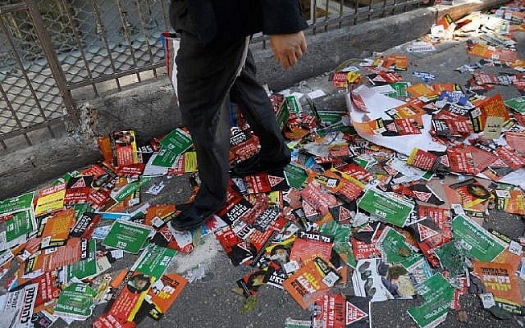 Un homme marche sur les prospectus électoraux qui jonchent une rue de Jérusalem en amont du scrutin municipal, le 28 octobre 2018 (Crédit : MENAHEM KAHANA / AFP)