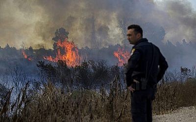 Un policier israélien regarde un incendie déclenché par un ballon transportant un tissu en feu, lancé par des Palestiniens de la bande de Gaza dans la réserve naturelle de Karmia, le jeudi 11 octobre 2018 (Crédit : AP/Tsafrir Abayov)