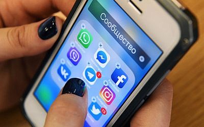 Illustration : Une femme tenant un smartphone sur lequel sont affichées les icônes des réseaux sociaux Facebook, Instagram, Twitter, etc., à Moscou, le 23 mars 2018. (Crédit : Kirill Kudryavtsev/AFP)