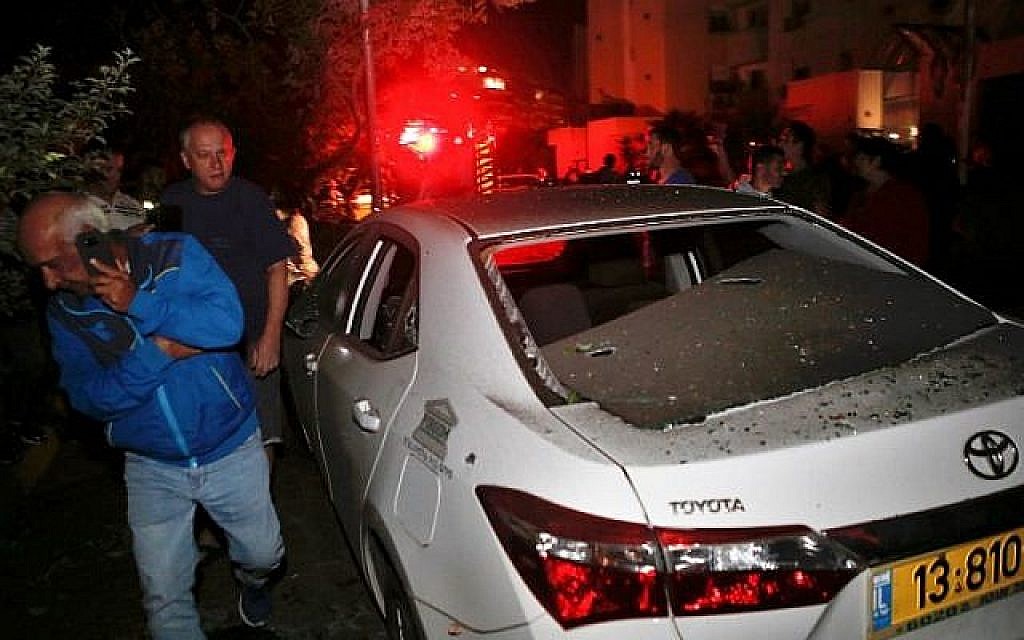 Deux hommes marchant devant un véhicule touché par une roquette tirée depuis la bande de Gaza, dans la ville d'Ashkelon, dans le sud d'Israël, le 12 novembre 2018. (Crédit : GIL COHEN-MAGEN / AFP)