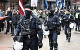 Des policiers encadrent des vétérans de la Légion lettone, une force commandée par les Waffen-SS nazis allemands pendant la Seconde Guerre mondiale, dont les sympathisants portent des drapeaux et des affiches en se rendant le 16 mars 2019 au Monument de la liberté à Riga, en Lettonie, pour commémorer une bataille clé en 1944, au terme de leur tentative avortée pour arrêter une avancée des Soviétiques. (Ilmars ZNOTINS / AFP)