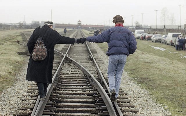 Un couple se tient la main en marchant en équilibre sur les rails de la voie ferrée ayant transporté plus d'un million de personnes vers la mort, au camp de concentration d'Auschwitz-Birkenau, le 26 janvier 1995. (Crédit : AP/Jockel Finck) Un couple se tient la main en marchant en équilibre sur les rails de la voie ferrée ayant transporté plus d'un million de personnes vers la mort, au camp de concentration d'Auschwitz-Birkenau, le 26 janvier 1995. (Crédit : AP/Jockel Finck)