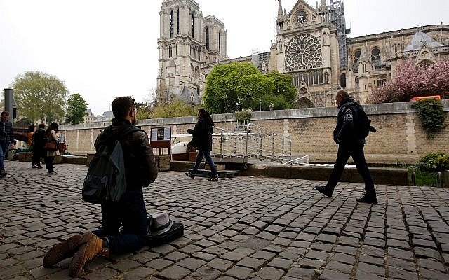 Un homme s'agenouille sur les quais de Seine face à la cathédrale Notre-Dame, le 16 avril 2019. (AP Photo / Christophe Ena)