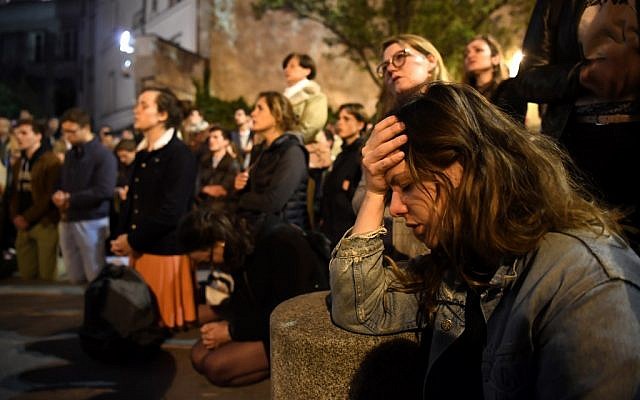 La foule à genoux sur le trottoir alors qu'ils prient devant la cathédrale Notre-Dame de Paris, le 15 avril 2019, alors que l'église était victime d’un incendie. (Eric Feferberg / AFP)