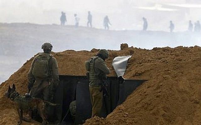Des soldats israéliens se rassemblent sur une position le long de la frontière avec la bande de Gaza, près du kibboutz de Nahal Oz, au sud d'Israël, le 30 mars 2019, alors que des Palestiniens (en arrière-plan) manifestent pour le premier anniversaire des manifestations de "La Marche du retour". (Jack Guez/AFP)