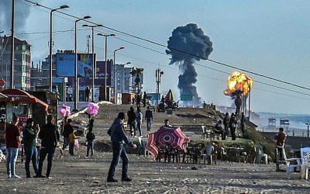 Des Palestiniens se réunissent sur la plage de Gaza City alors que des fumées et des flammes s'élèvent suite aux attaques israéliennes qui ont suivi les tirs de roquette des groupes terroristes palestiniens, le 4 mai 2019 (Crédit : Sami al-Sultan/AFP)